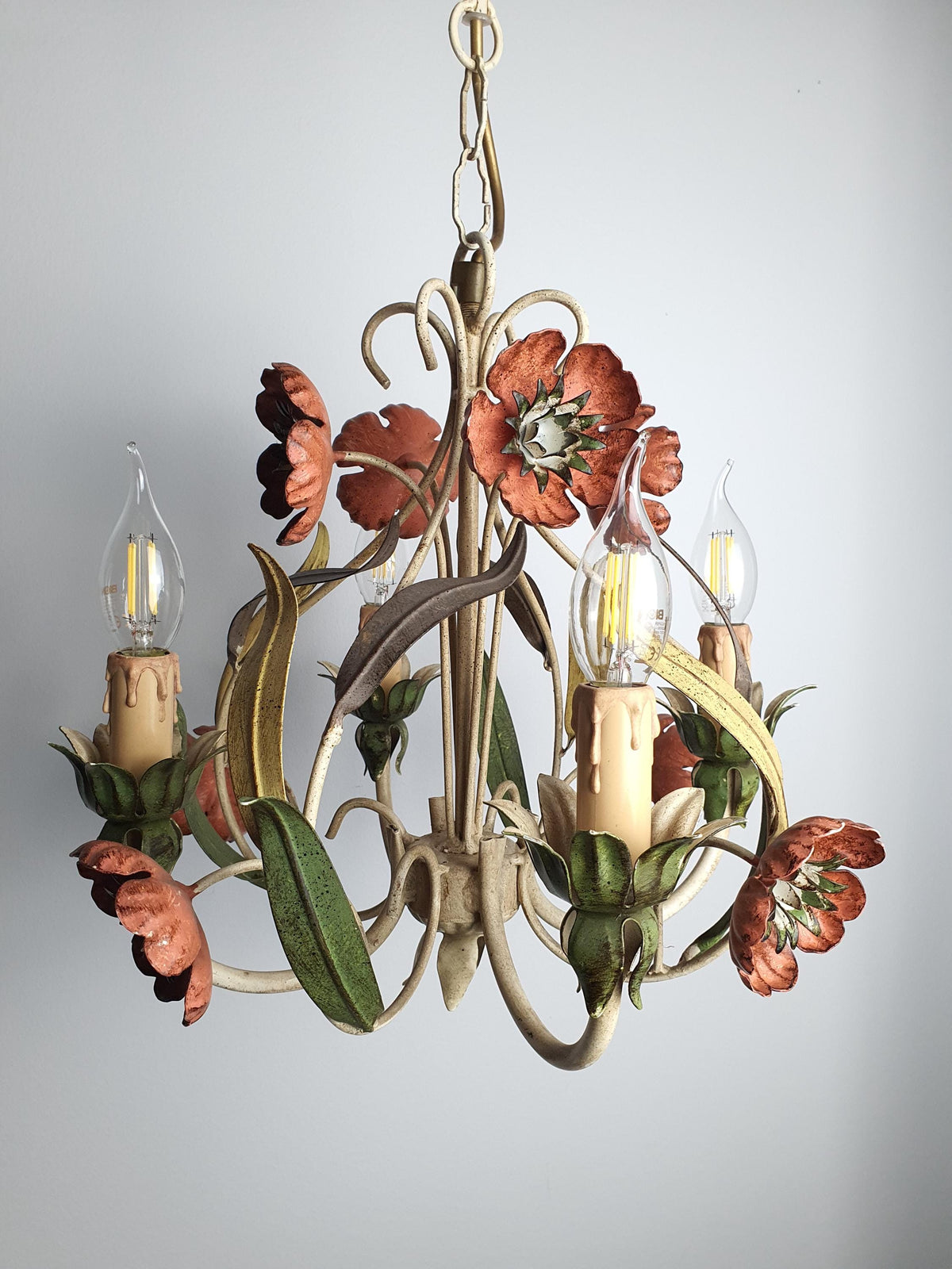 Vintage Italian tole chandelier lit, warm candle-style glow through red poppy flowers and green leaves, painted tole metal