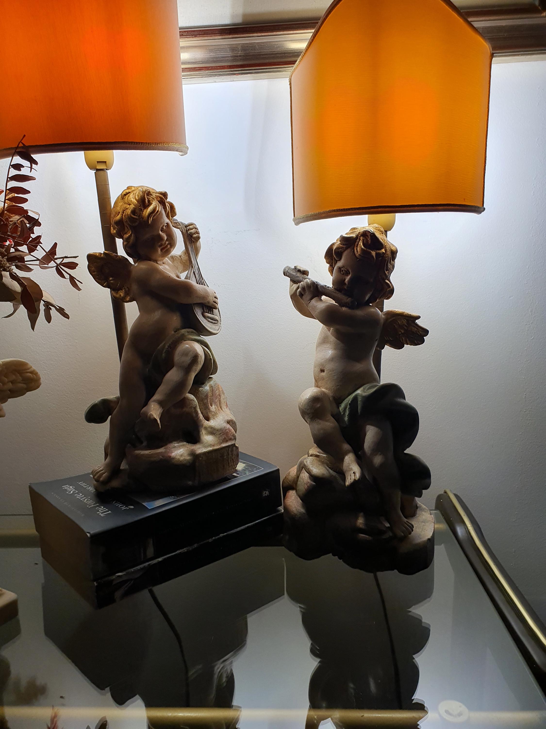 Pair of Italian cherub angel table lamps lit, warm ambient glow through fabric shades, romantic interior