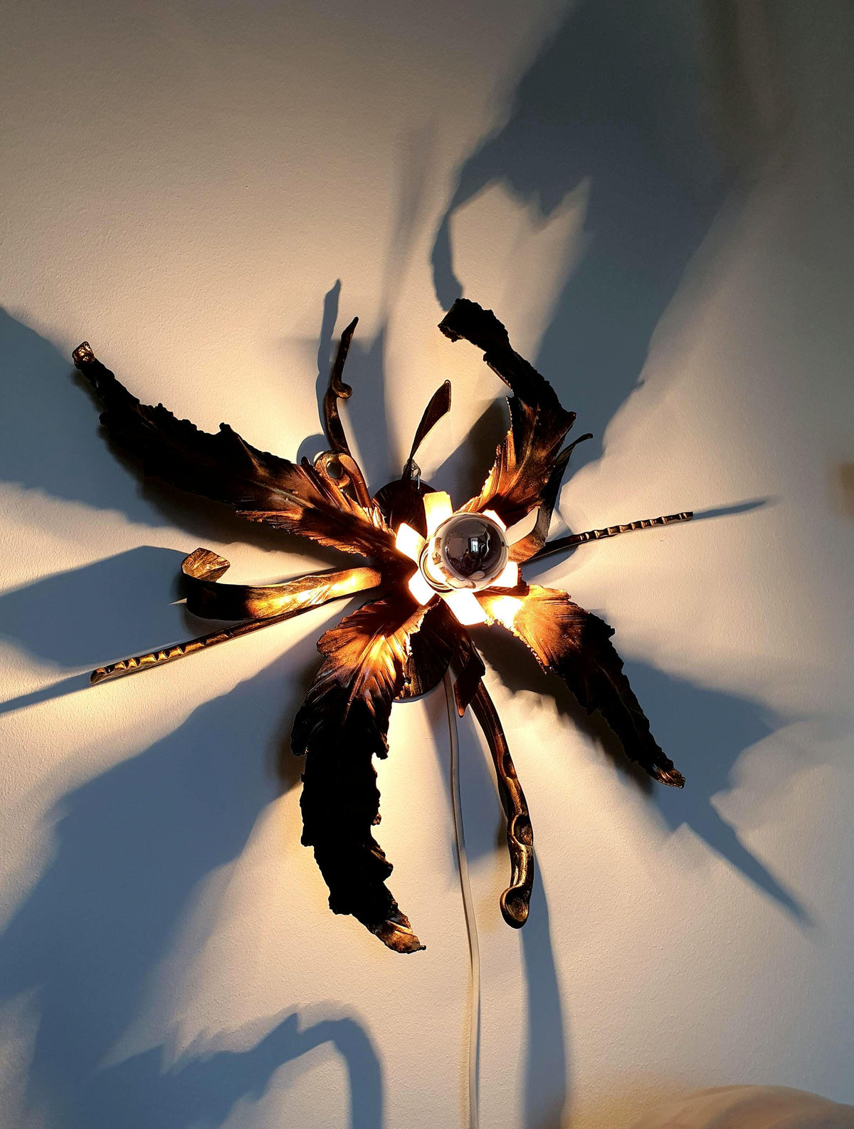 Handcrafted botanical light with flowing metal leaves and layered organic forms
