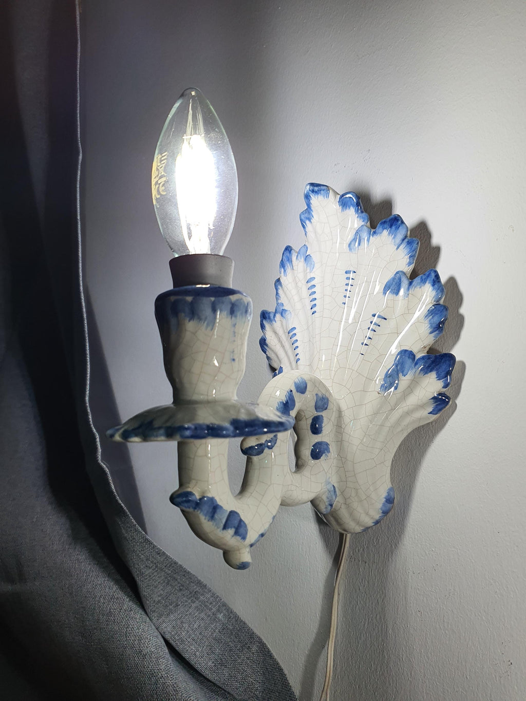 Pair of vintage Italian Bassano ceramic wall sconces lit, warm soft glow, white glaze and blue hand-painted details, cottage interior
