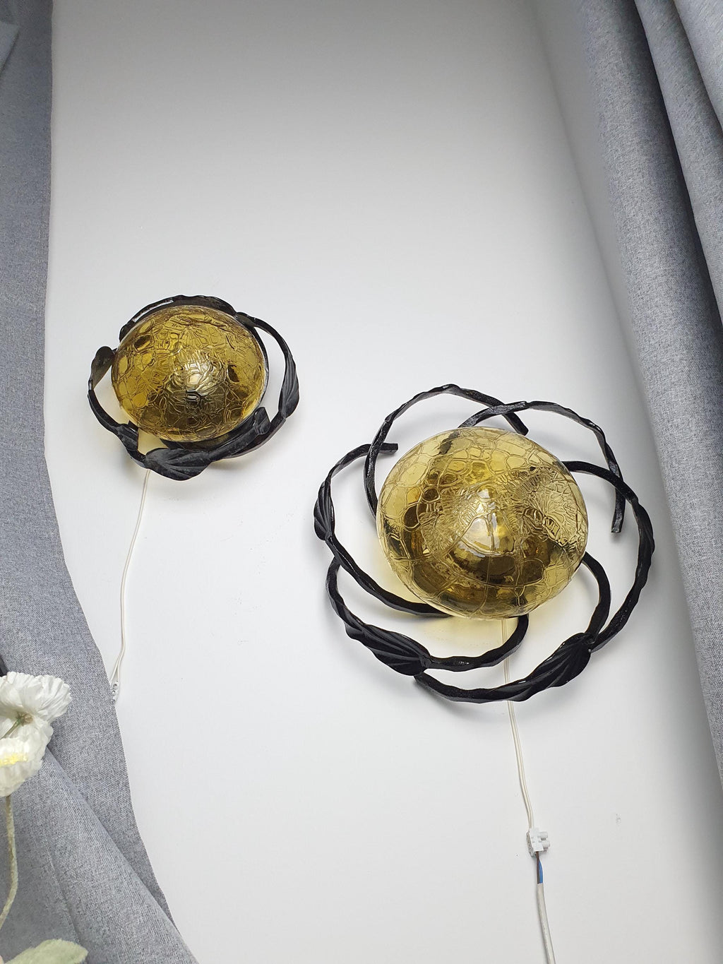 Vintage 1970s Brutalist wrought iron wall sconce unlit, showing sculptural leaf iron silhouette and honey amber glass diffuser

