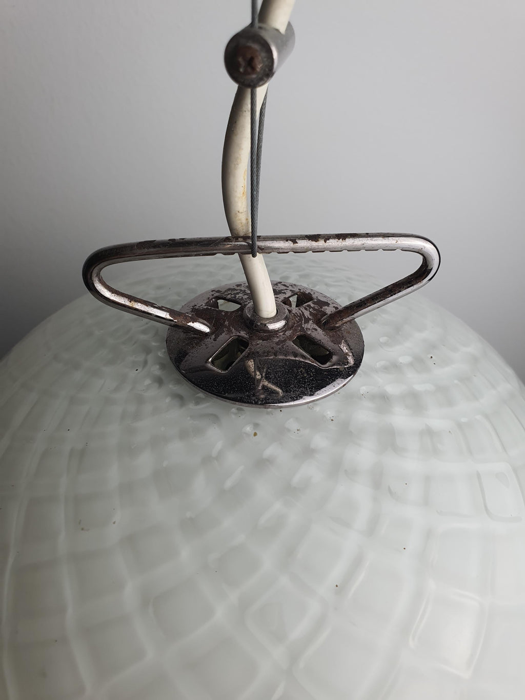 Oxidation on the dark chrome hardware of a vintage glass pendant
