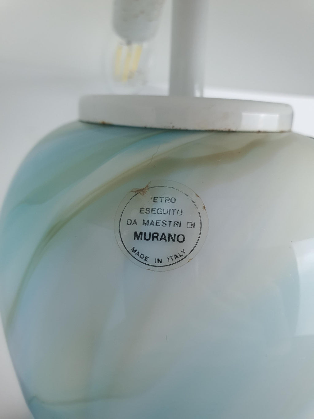 Close-up of the original Murano glass label on the lamp base, confirming authentic Murano, Italy provenance, with the bulb socket fitting visible above.
