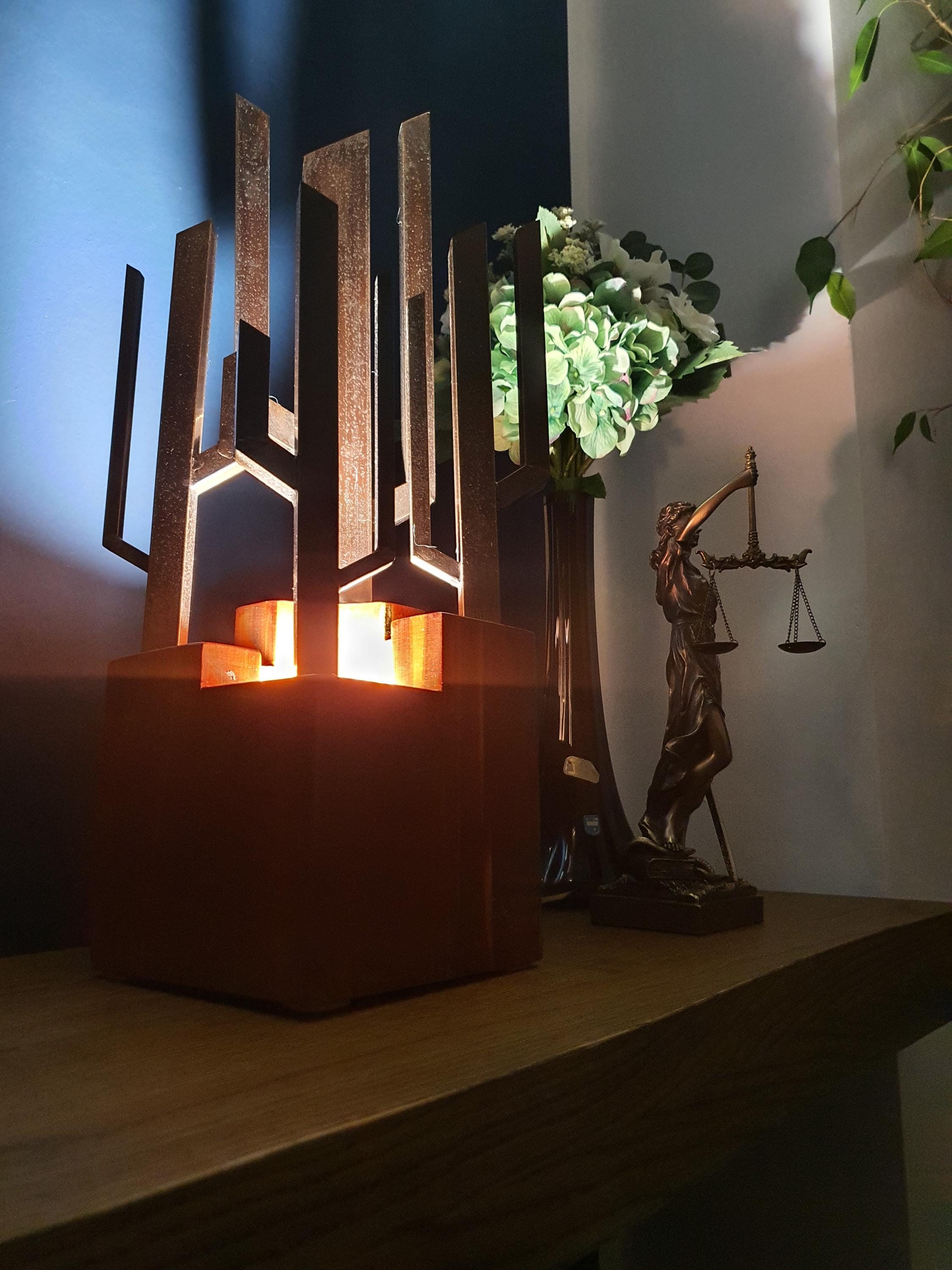 Signed Carlo Brutalist table lamp lit, dramatic shadows cast by vertical metal elements, warm wood base glow
