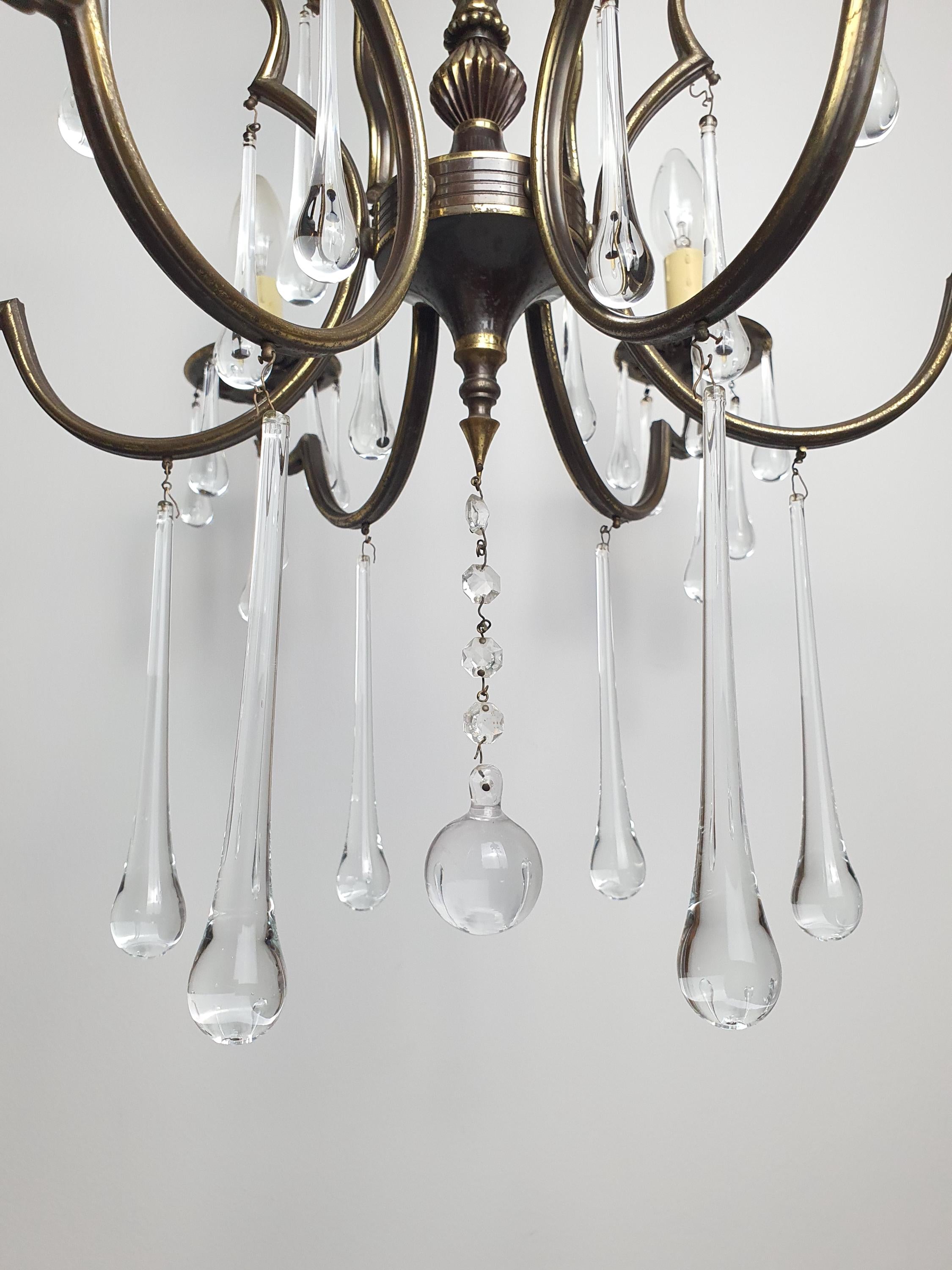 Close-up of clear Murano glass teardrop pendants on vintage Italian brass chandelier, crystal-clear drops, multiple sizes

