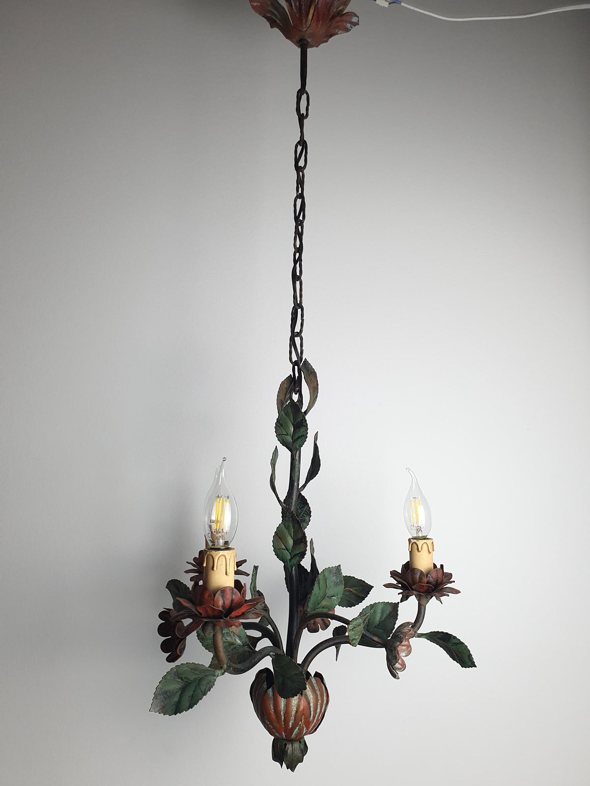 Green painted metal foliage surrounding three candle-style chandelier arms
