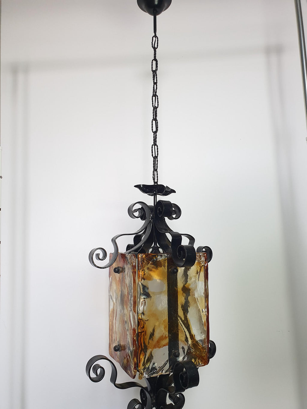 Mazzega style Murano pendant lit, warm golden amber glow, dramatic dark shadows, black wrought iron frame, high ceiling setting