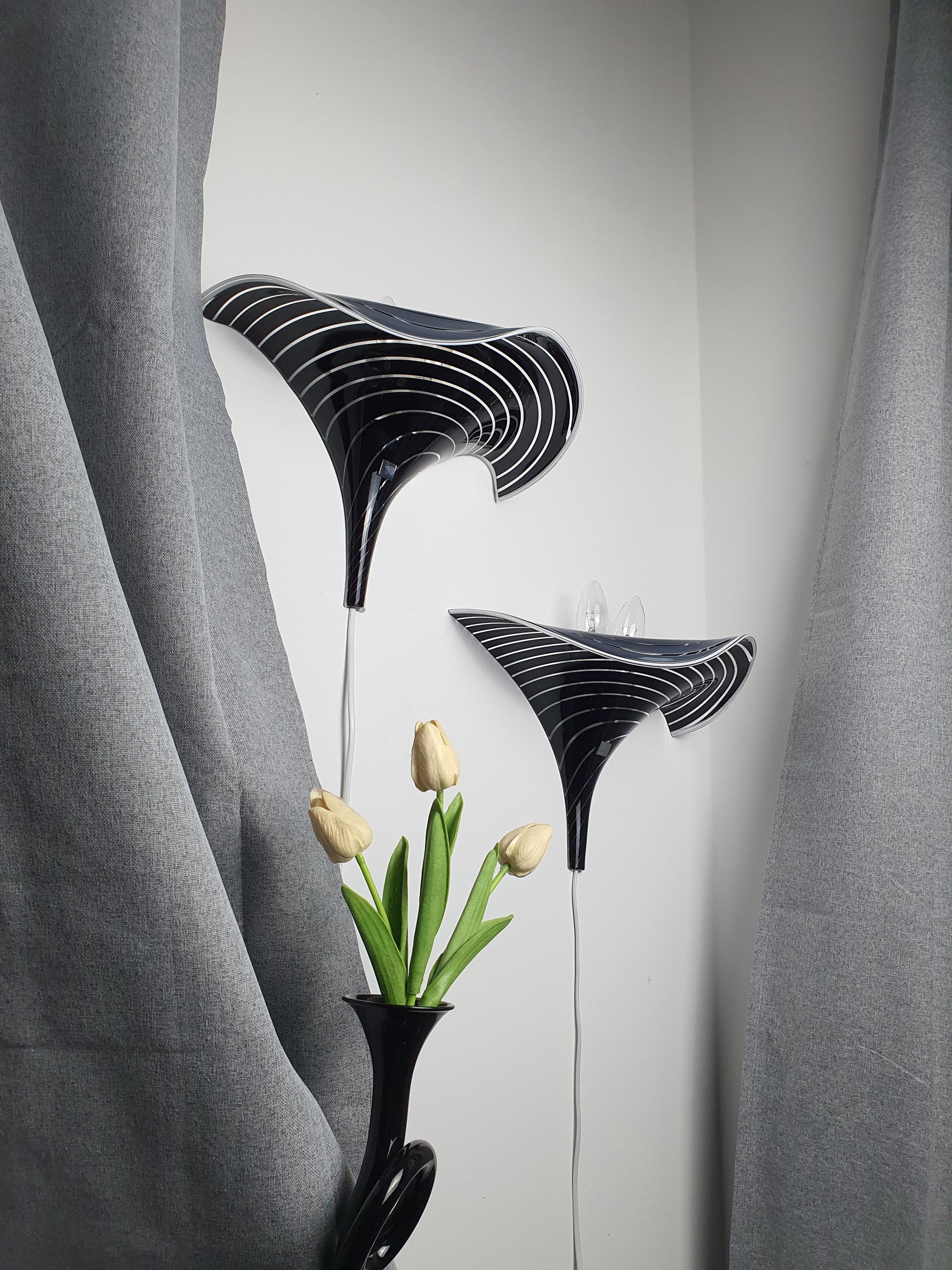 Pair of vintage Murano calla lily wall sconces lit, dramatic black and clear zebra stripe glow, wave form, moody interior