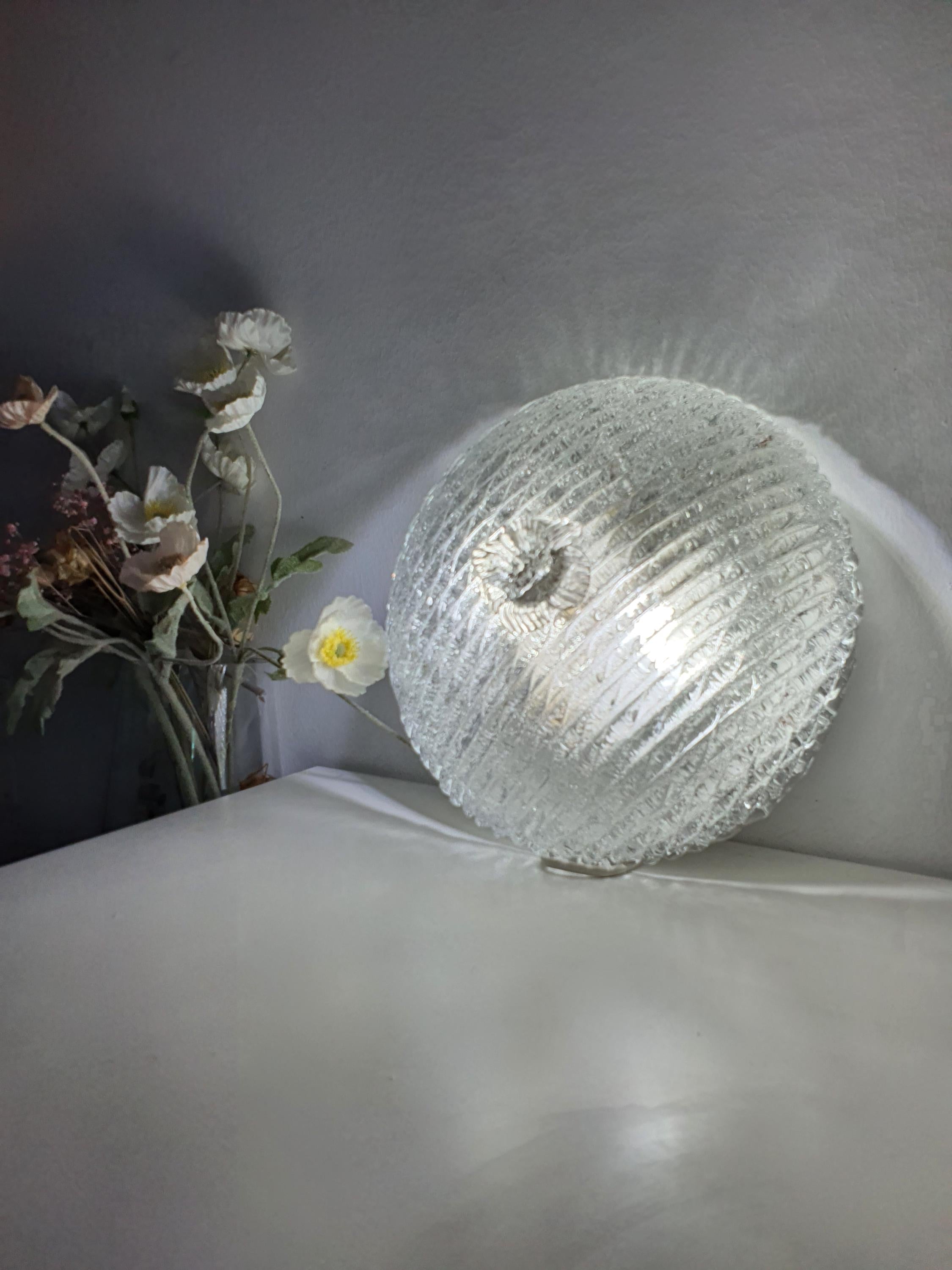 Vintage Murano ribbed shell flush mount lit, luminous iced glass reflections, warm brass base contrast, Art Deco MCM interior