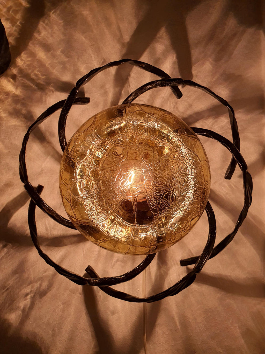 Vintage 1970s Brutalist wrought iron wall sconces lit, warm golden honey amber glow through textured glass, dark iron leaf frame

