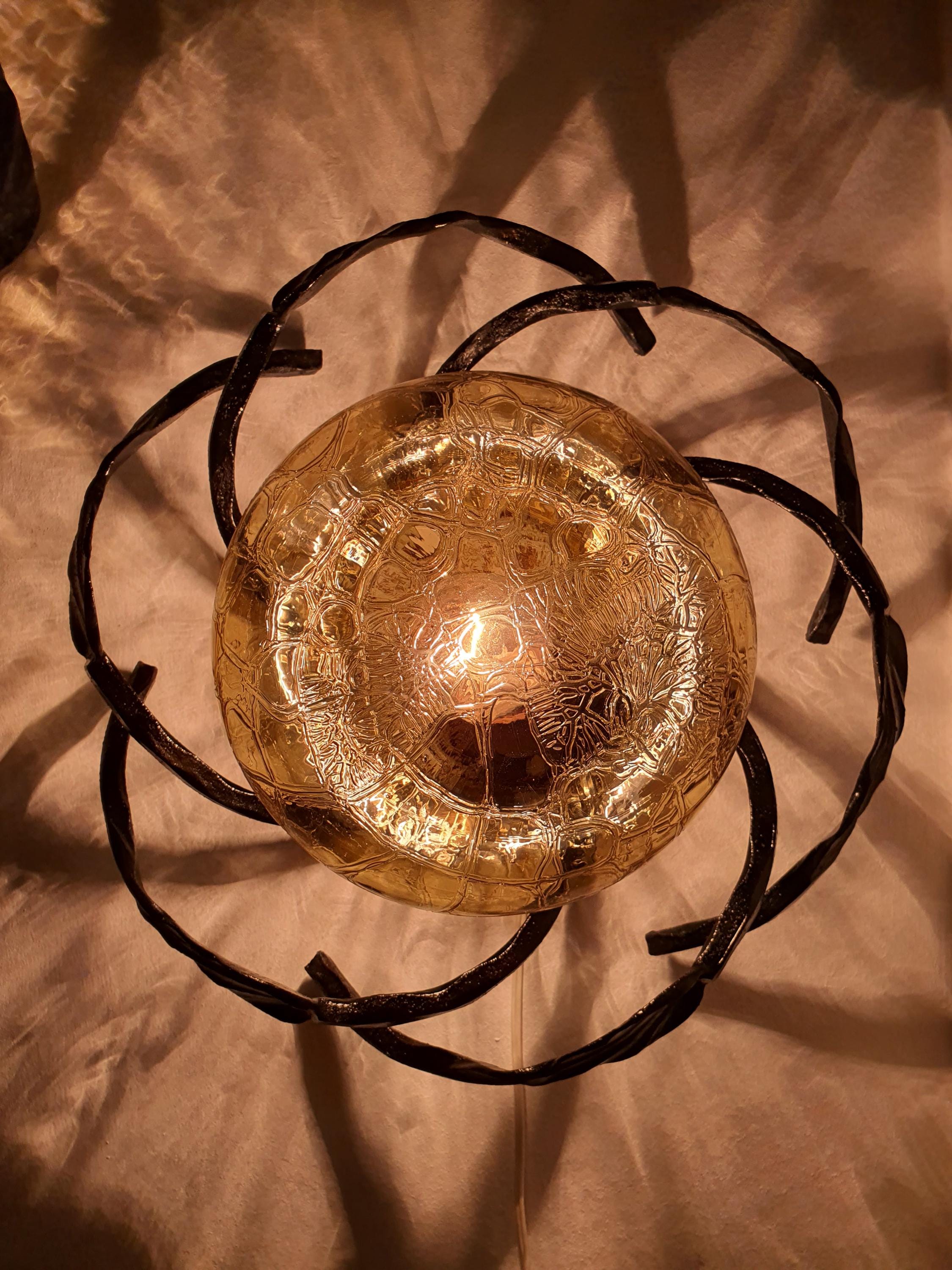 Vintage 1970s Brutalist wrought iron wall sconces lit, warm golden honey amber glow through textured glass, dark iron leaf frame

