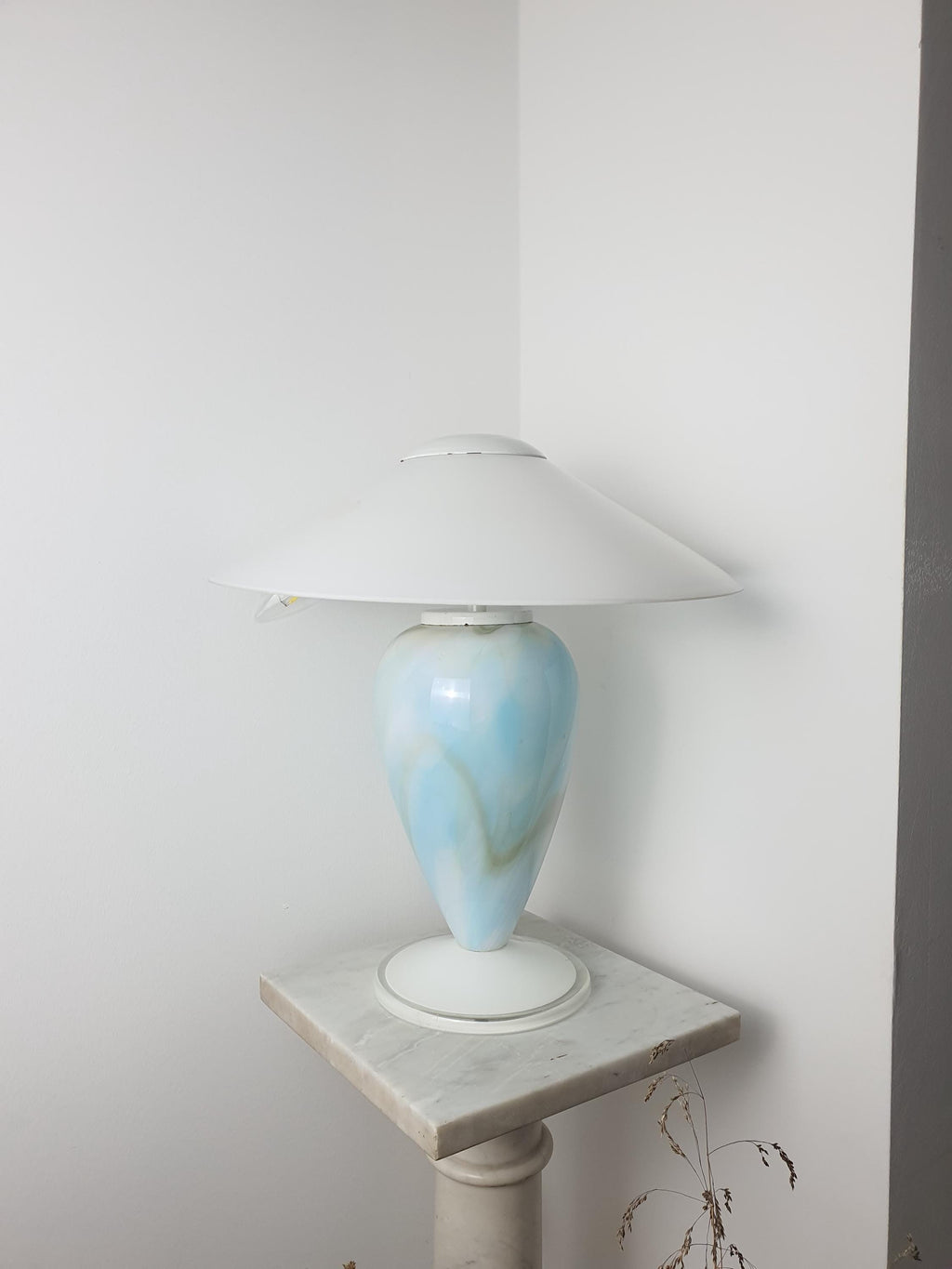 Unlit sky blue marbled Murano glass mushroom table lamp with white glass shade, photographed in natural light on a marble pedestal in a room corner.