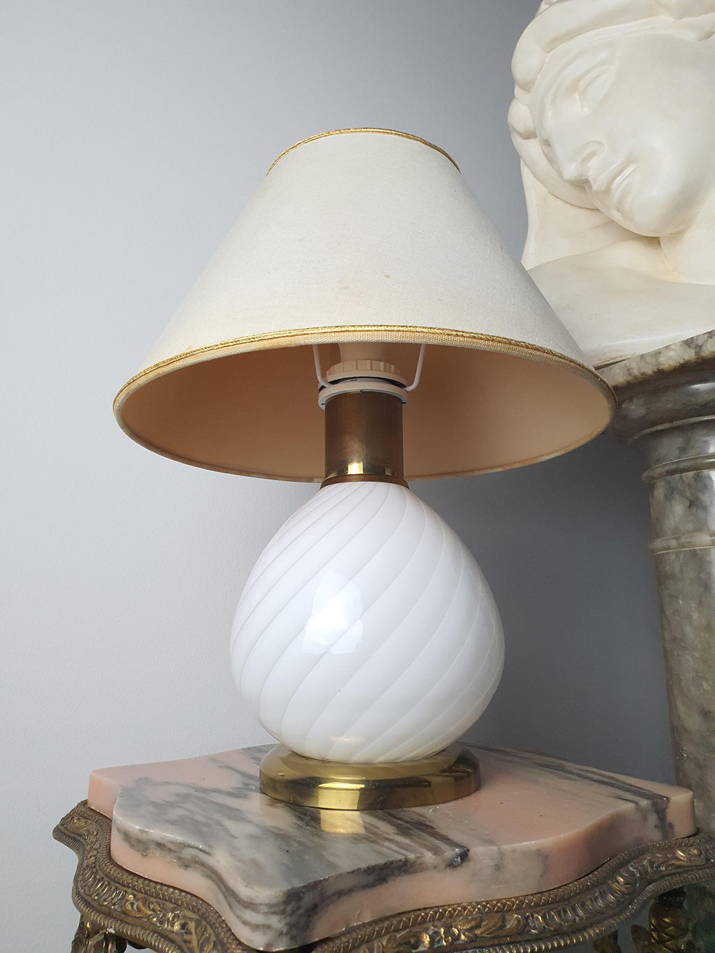 Vintage Murano white candy swirl bedside lamp lit, warm cosy glow through beige textile shade, brass base, bedroom setting