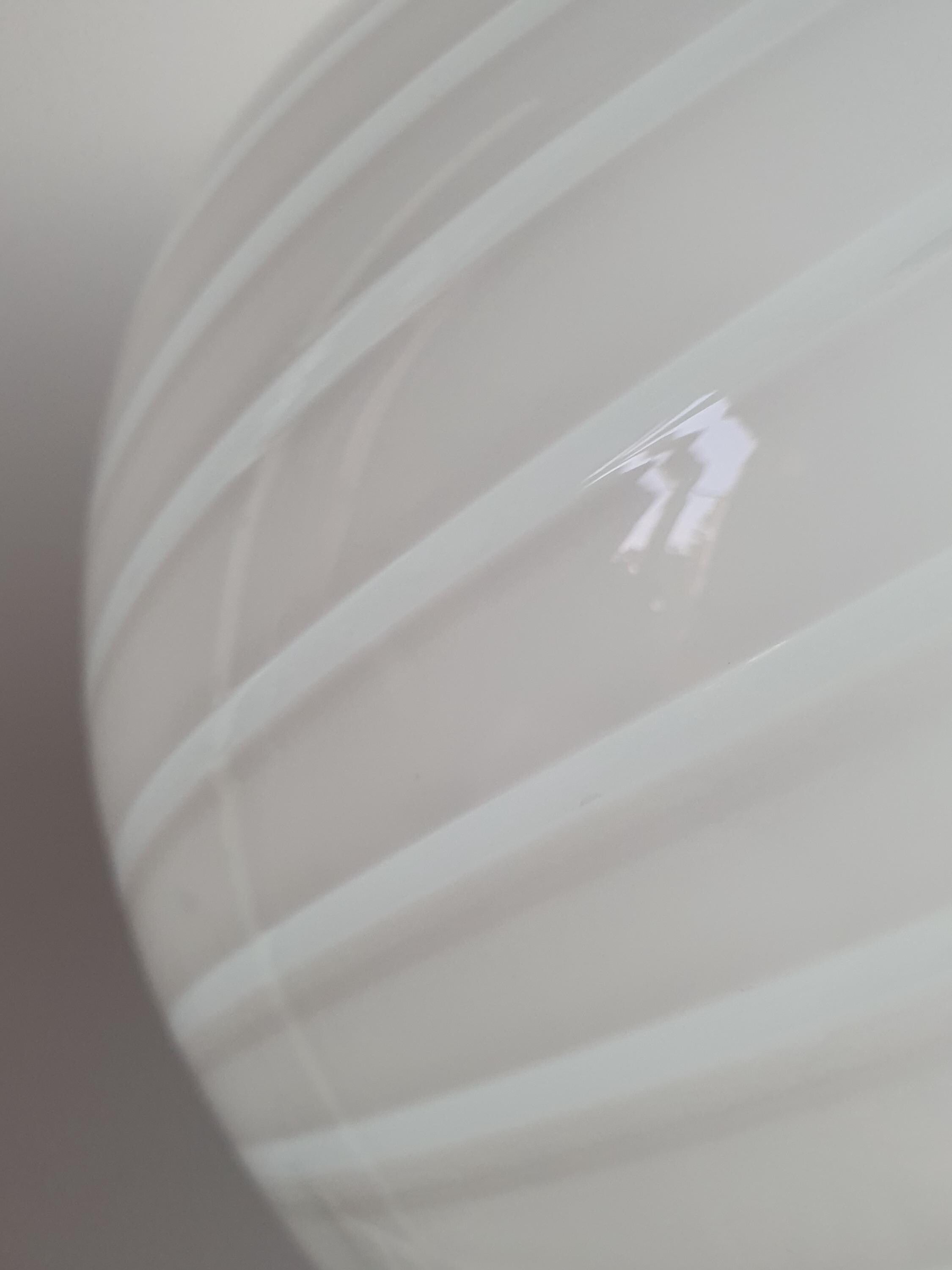 Vintage Murano white swirl globe pendant lit, soft warm diffused glow through white swirl glass, dining room setting

