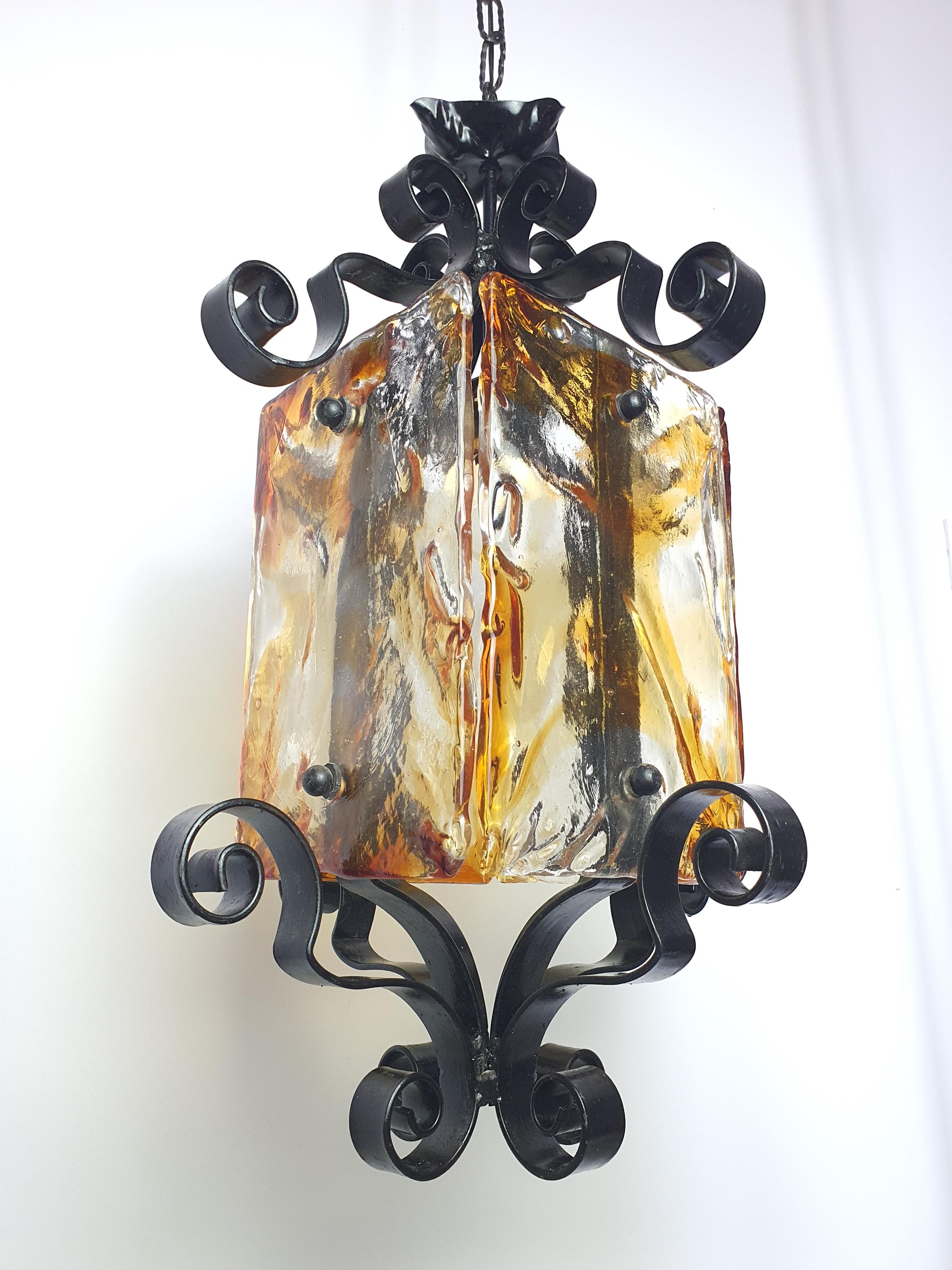 Mazzega style Murano pendant in dining room, warm amber golden glow, black iron frame, rustic medieval high ceiling interior