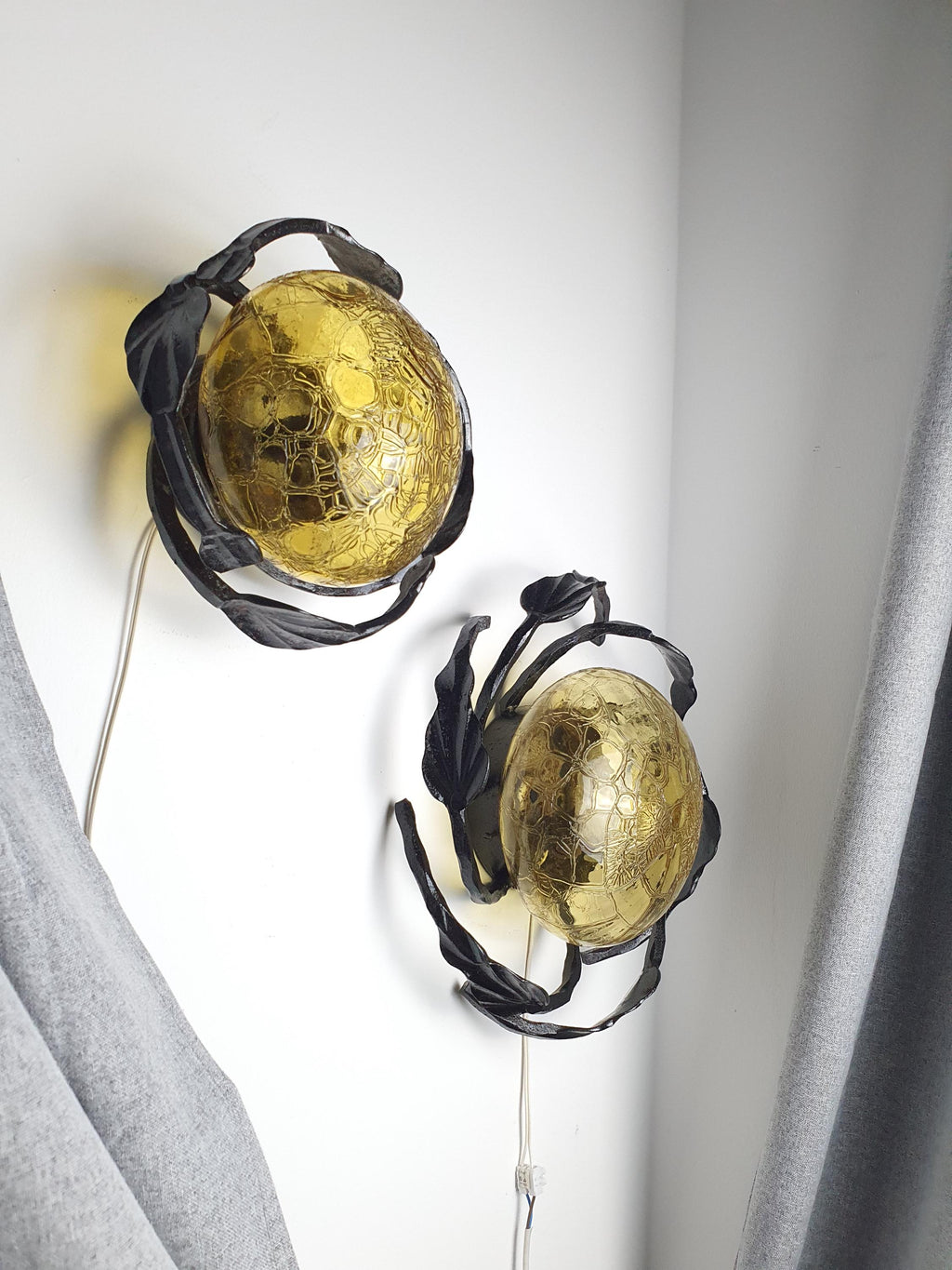 Pair of vintage 1970s Brutalist wrought iron wall sconces installed together, large and small, honey amber glow, rustic interior

