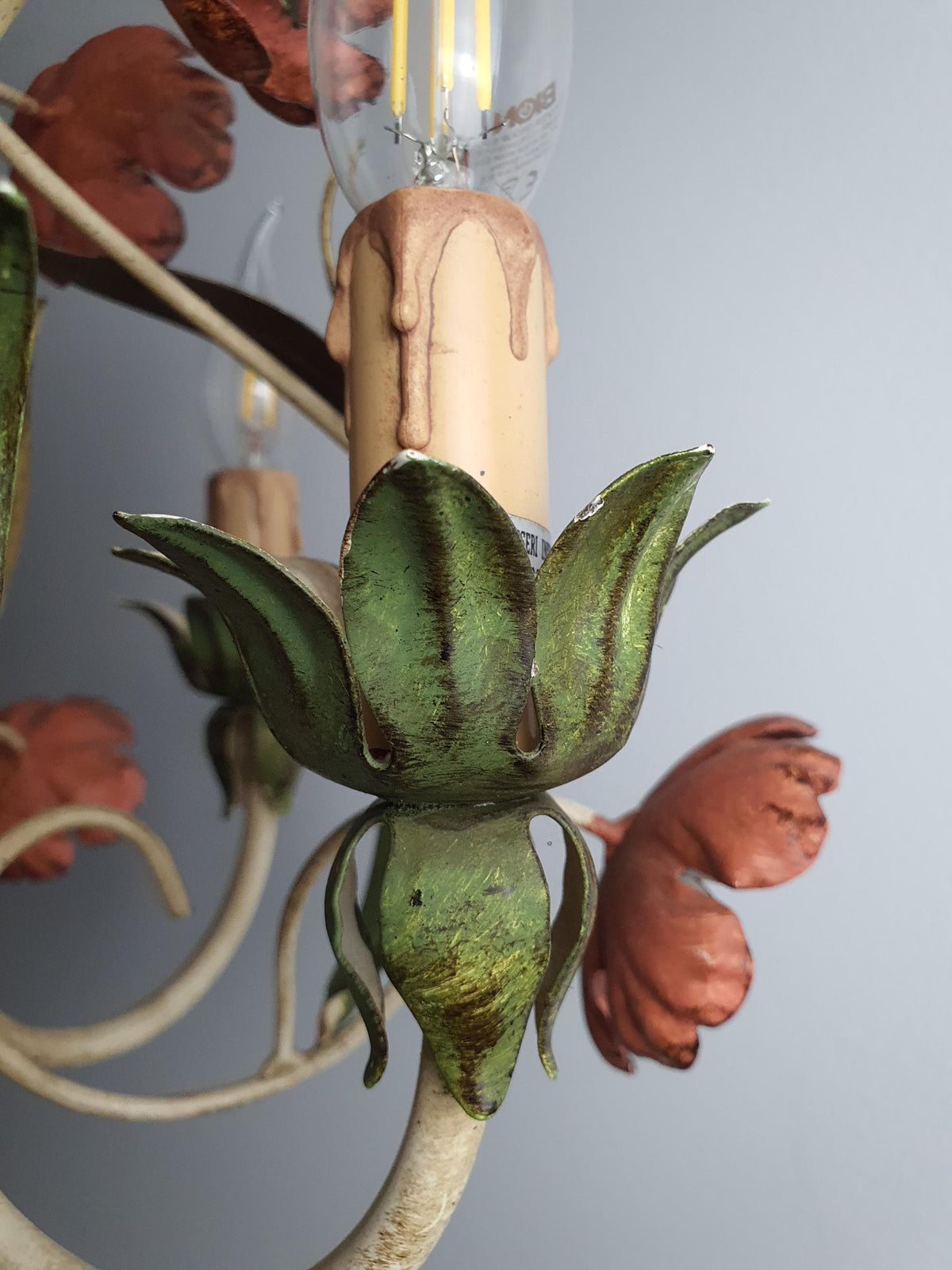 Close-up of handcrafted red poppy flowers and green leaves on vintage Italian tole chandelier, painted metal botanical detail
