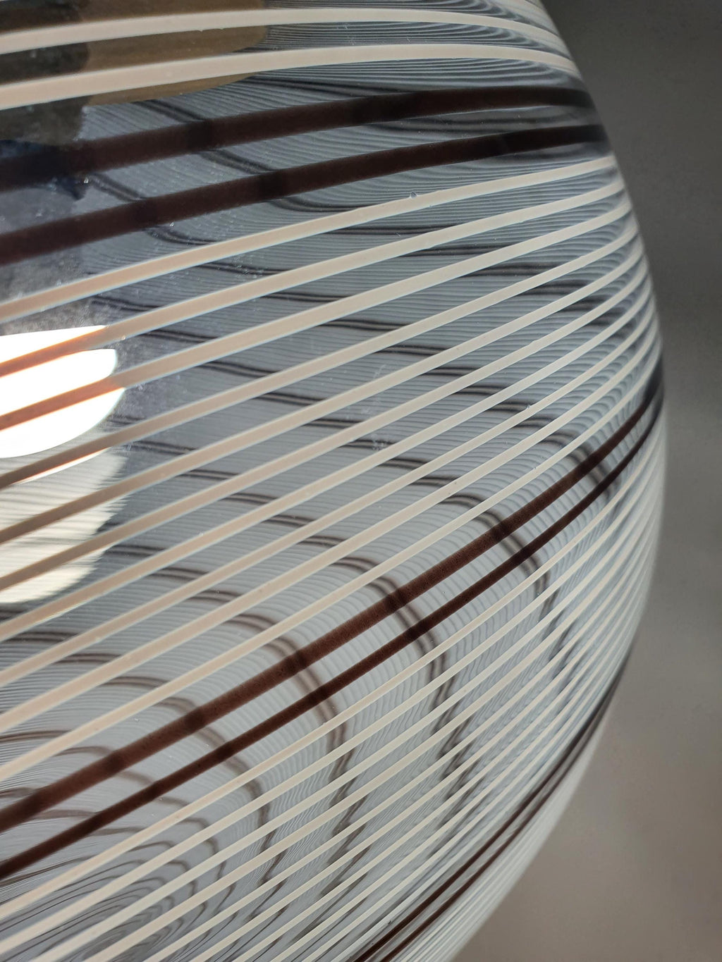 Clear spherical glass shade decorated with swirling white and brown lines
