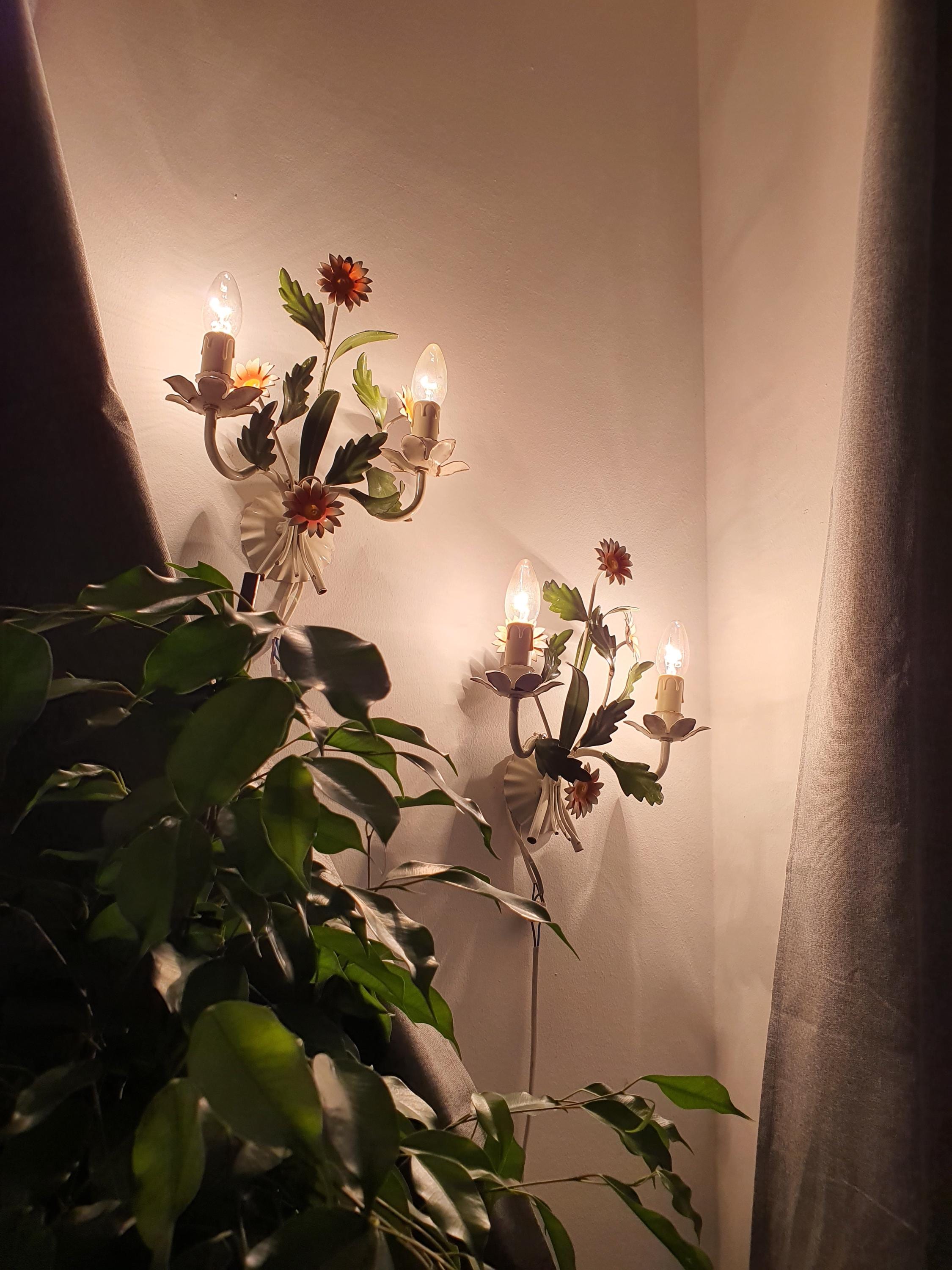 Pair of vintage 1970s Italian tole wall sconces lit, warm floral glow, white green orange painted metal, Mediterranean interior