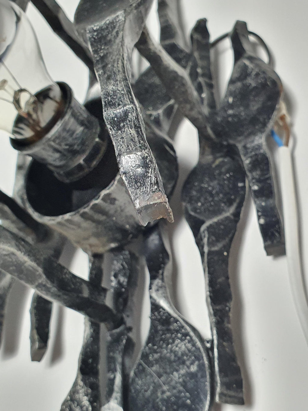 Brutalist iron wall sconce front view, vertically layered torch elements, chrome bulb holder